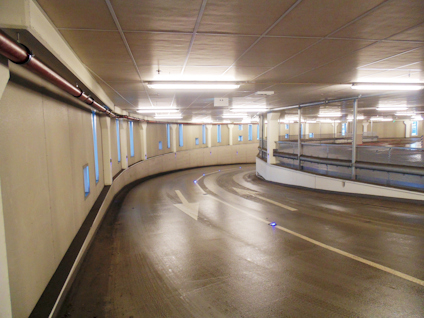 Parkeringshus med våt golv, markerad körbana och pil för trafikriktning.